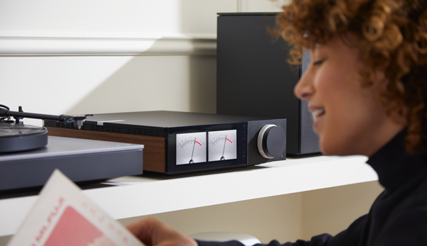 Update beim Evo 150 & Evo 75 | Evo-Gerät mit aktivierter VU-Meter-Anzeige auf einem Regal zwischen einer Lautsprecherbox und einem Plattenspieler, eine unfokussierte Person die liest ist erkennbar im Vordergrund